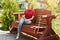 Carefree female with straight hair wearing red sweater and trendy jeans sitting at comfortable wooden bench in park enjoying sunsh