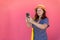 Carefree girl stands near a pink wall in the street taking a selfie