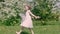 Carefree girl teenager in white dress running on flowering meadow in fruit garden at sunny day. Running girl jumping on