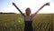 Carefree hippie girl in dress standing on green barley field and raising hands at sunset. Happy punk woman with tattoos