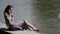 carefree middle-aged woman is talking by cell phone sitting on shore of lake in city park
