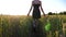 Carefree punk girl with tattoos walking through green barley field at sunset. Young hippie woman in dress going among