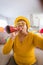 Carefree senior woman in shutter glasses blowing party horn during video call at home