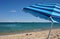 Carefree vacation: striped beach umbrella, flip-flops on the sand and bright blue sea