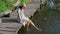 Carefree woman in a dress and hat dangles her feet in the water while sitting on the pier in a sunny day. Beautiful girl