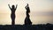 Carefree women in long black dress dancing on beach at sunset