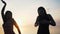 Carefree women in long black dress dancing on beach at sunset