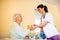 Careful young nurse brings water to senior woman