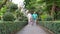 A caregiver helps support an elderly Asian woman holding a walking cane for exercise in a park.