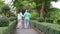 A caregiver helps support an elderly Asian woman holding a walking cane for exercise in a park.