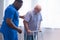 Caregiver is teaching old man to walk with walker. Professional nurse and patient in a nursing home. Assistance