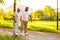 Caregiver is teaching old man to walk with walker. Professional nurse and patient walking outdoor at sunset. Assistance