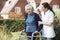 Carer Helping Senior Man To Walk In Garden Using Walking Frame