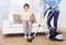 Caretaker cleaning floor while senior woman sitting on sofa