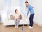 Caretaker cleaning floor while woman sitting on sofa