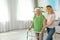 Caretaker helping elderly  with walking frame indoors