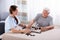 Caretaker Looking At Elder Man Playing Dominoes