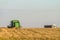 Cargo heavy grain carrier and green harvester working in the field