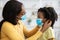 Caring Black Mother Putting On Face Mask On Her Little Daughter