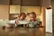 Caring brother pouring milk into a bowl of cereal while preparing breakfast, sitting together with his sister at the