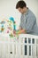 Caring father assembling baby`s cot and putting toy carousel in