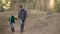 Caring father is hiking with his child in forest on sunny autumn day, man and boy are walking and talking holding hands