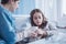 Caring mother giving hot tea to sick daughter in the clinic