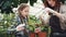Caring mother professional gardener is teaching her daughter to hoe soil in plant pot with small shovel and talking to