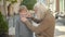 Caring old Caucasian man adjusting shirt of smiling little boy on city street. Thankful grandson hugging grandfather and