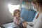 Caring young Caucasian mother in a medical mask sits on an airplane and puts on a mask for her child. vacation in asia