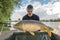 Carp fishing. Fisherman with fish trophy in hands at lake