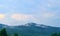 Carpathian mountains and cloudy blue sky. Nature background with mountain silhouettes and forest trees in mist. Travel background.