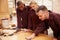 Carpenter With Apprentices Finishing Wood In Workshop