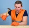 Carpenter concept. Man, handyman in working uniform and protective gloves handcrafting, light blue background. Carpenter