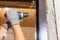 The carpenter drills holes in the wall and the metal door frame with a drill, later screws the screws and fastens the door frame