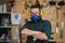 A carpenter in goggles, headphones and a respirator stands with his arms crossed over his chest in a workshop.