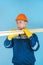 A carpenter in a hardhat and gloves carries a stack of boards on a blue background. Vertical photo