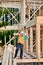 Carpenter holding large beam while builds wooden frame house near the forest.