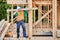 Carpenter holding large beam while builds wooden frame house near the forest.