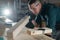 Carpenter measures a wooden board while working in a workshop.