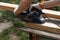 A carpenter planks wood with an electric plane. Woodworking carpentry. Close-up. Man in the garden sanding wooden planks