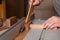 Carpenter sawing wooden plank by circular saw helping with stick