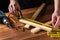 Carpenter or woodworker uses a construction tape to measure the length of a piece of wood. Hands of the master close-up at work.