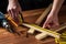 Carpenter or woodworker uses a construction tape to measure the length of a piece of wood. Hands of the master close-up at work.