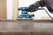 Carpenter working with electric sheet finishing sander on wood lath on desk, on background oriented strand board