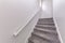 Carpeted stairs with wall-mounted white handrailing upstairs