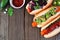Carrot hot dogs with assorted toppings, corner border on a wood background