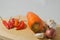 A carrot, red chilies, cloves of garlic, and an onion on a wooden cutting board