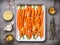 Carrots with thyme, garlic, lemon and honey on baking tray , cooking preparation with ingredients, top view. Healthy root vegetabl