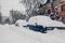 Cars covered with snow during snowfall in city. Automobiles stuck in heaps after winter blizzard